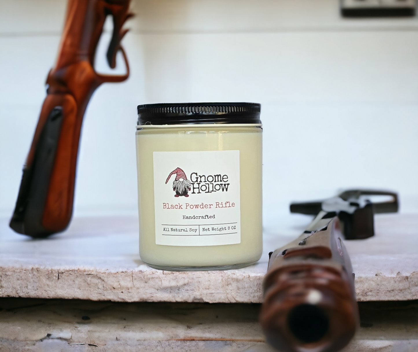 Black Powder Rifle Candle sitting on a white shelf with rifles to each side