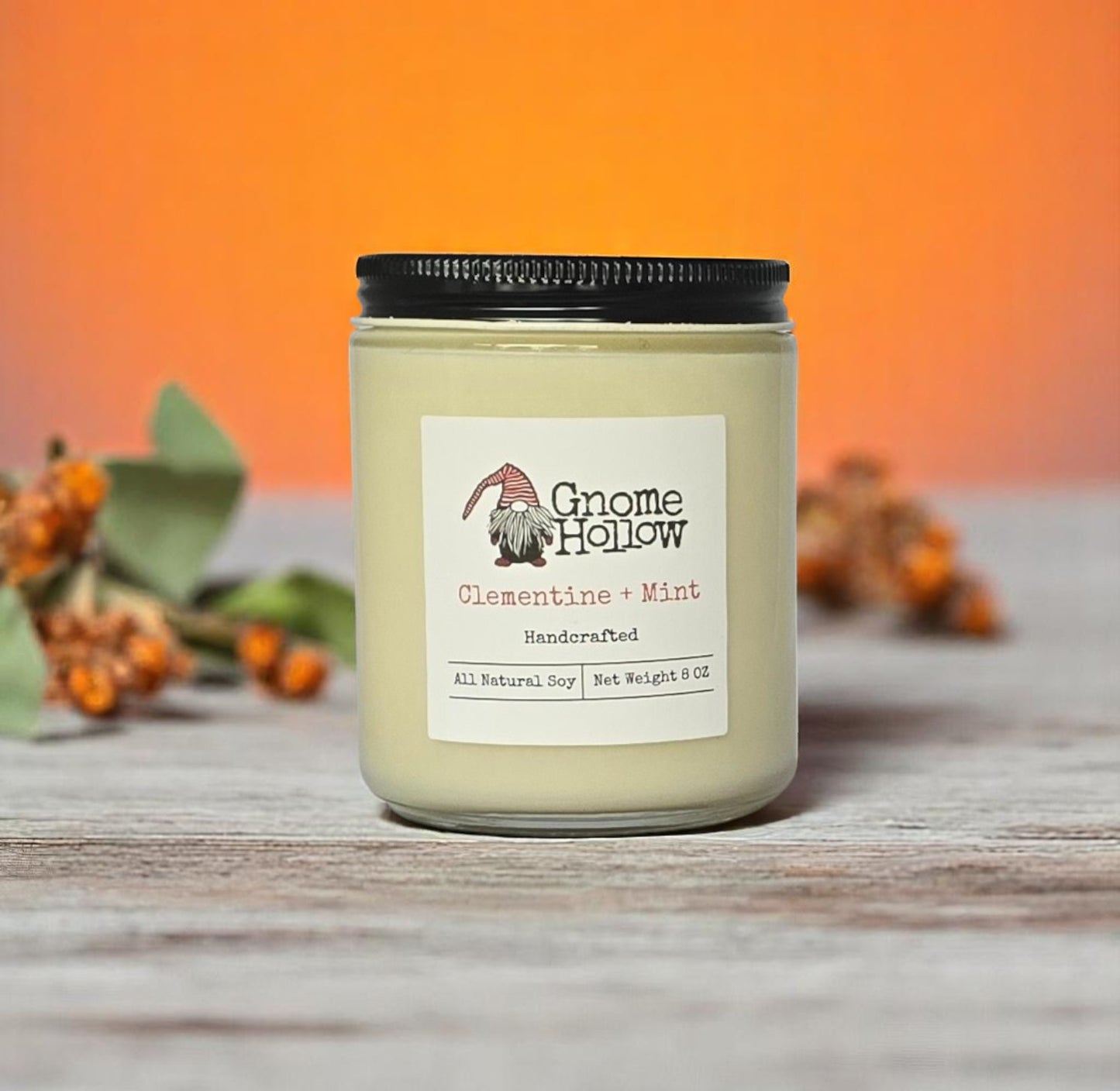 Clementine + Mint candle sitting on a wood surface with orange flowers displayed behind