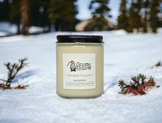 Frosted Juniper soy candle sitting in snow with a tree line in the background