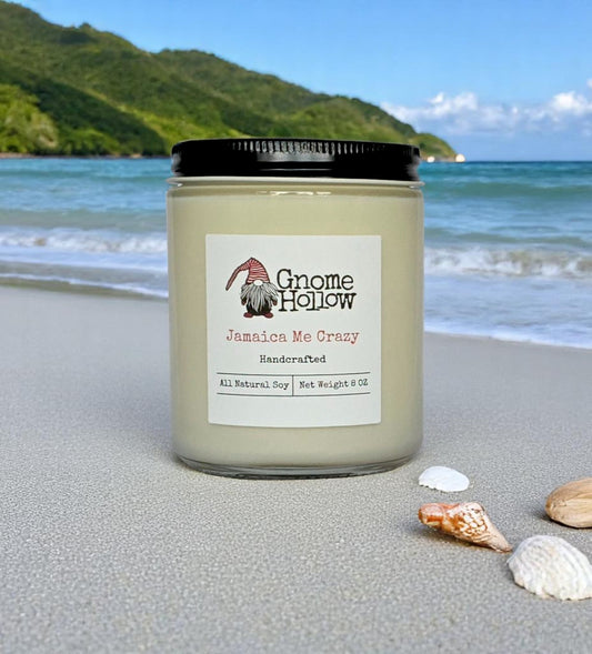 A candle with a label that reads 'Me Crazy candle placed on a sandy beach with a beautiful landscape in the background.