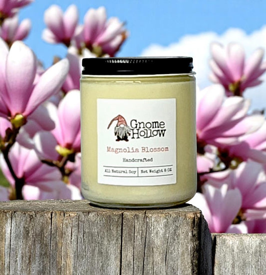 Magnolia Blossom candle set on a wooden surface with pink magnolia flowers in the background.