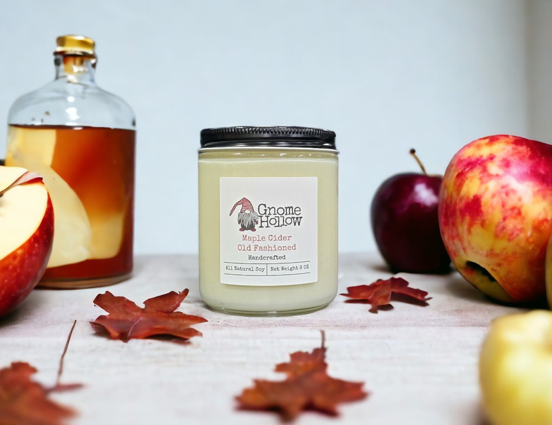 Maple Cider Old Fashioned candle sitting on a counter with apples and a bottle of bourbon