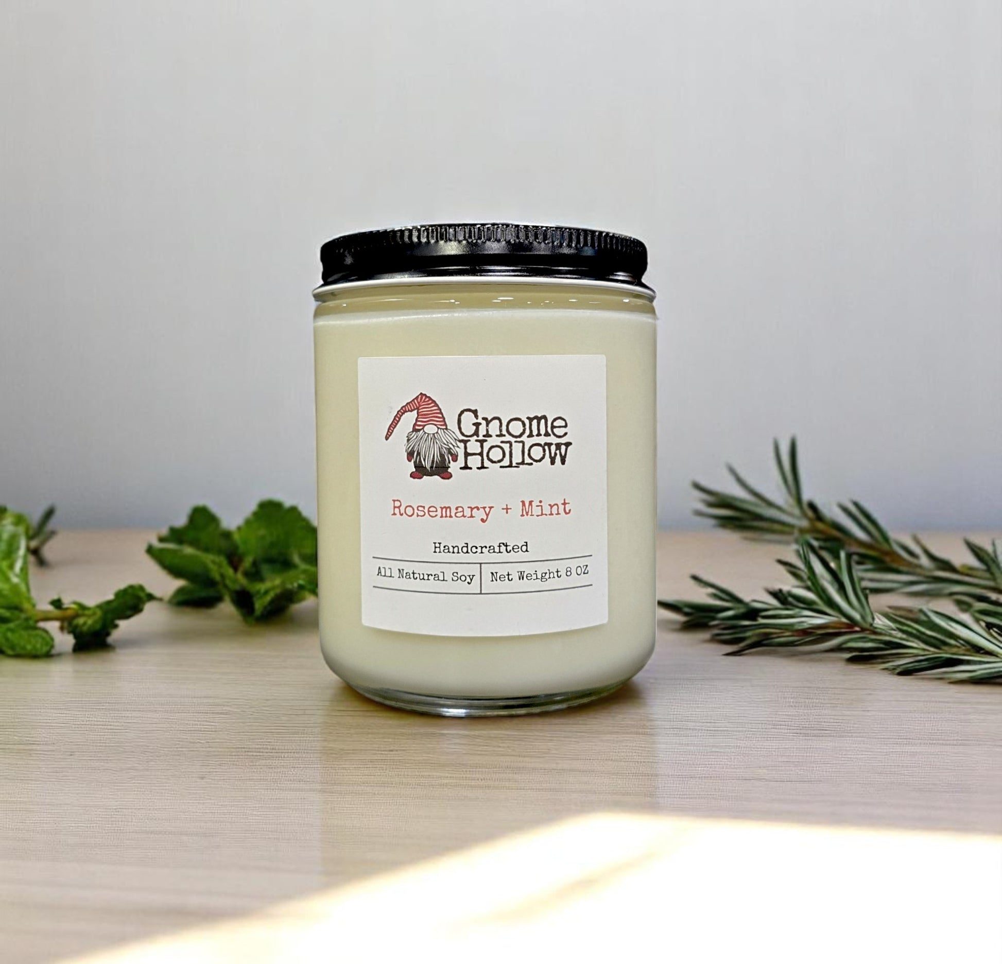 Gnome Hollow Rosemary & Mint candle sitting alongside some fresh rosemary and mint leaves.