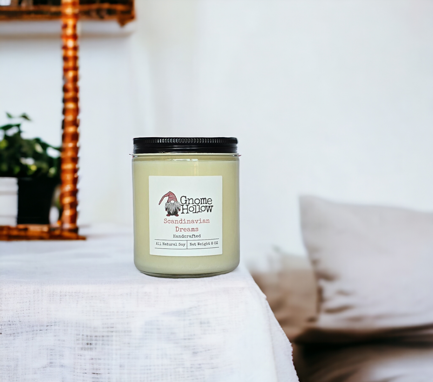 Scandinavian Dreams candle sitting on a bedside table with a lamp and pillows in the background