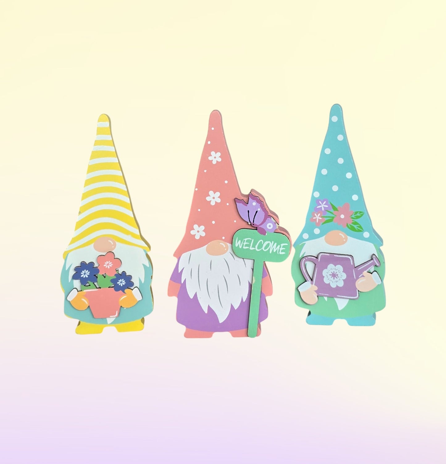3 wooden gnomes. One with a yellow striped hat, one with a pink hat with flowers, and the last hat is teal with white dots