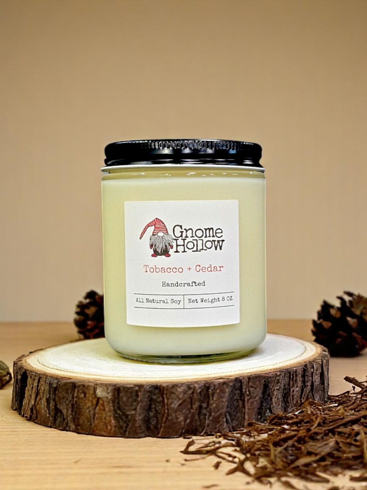 Tobacco + Cedar candle sitting on a sliced tree with pine cones & tobacco surrounding it