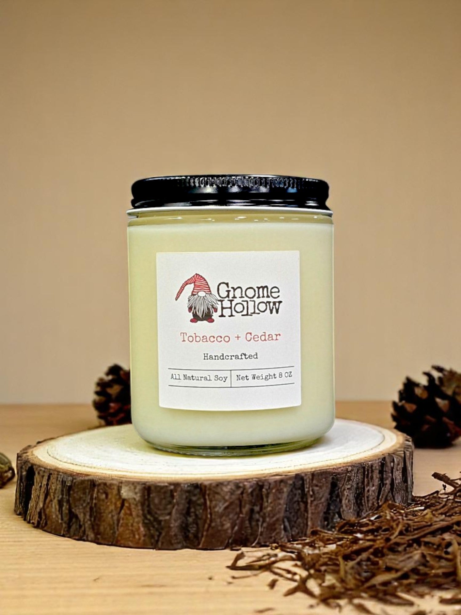 Tobacco + Cedar candle sitting on a sliced tree with pine cones & tobacco surrounding it