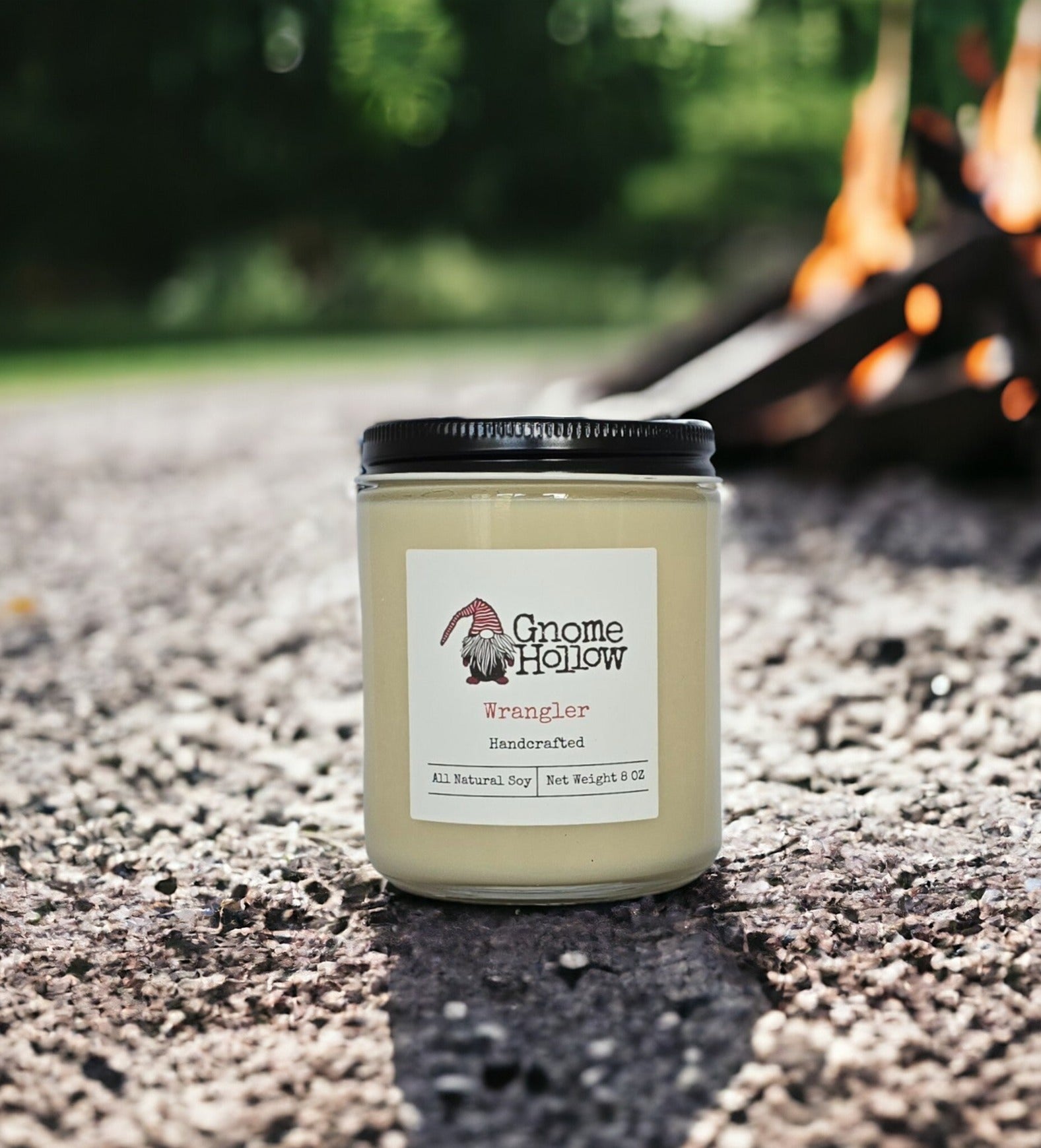 Wrangler candle sitting on a textured surface with a blurred campfire in the background