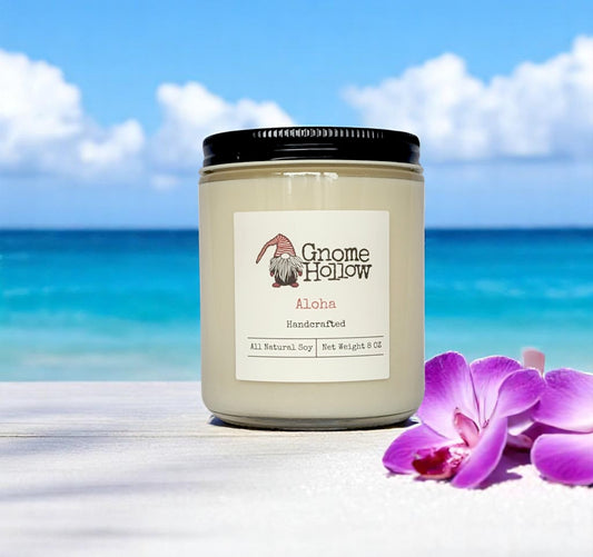  Aloha candles set on a sandy surface with a vibrant ocean and sky in the background, alongside a purple orchid flower.