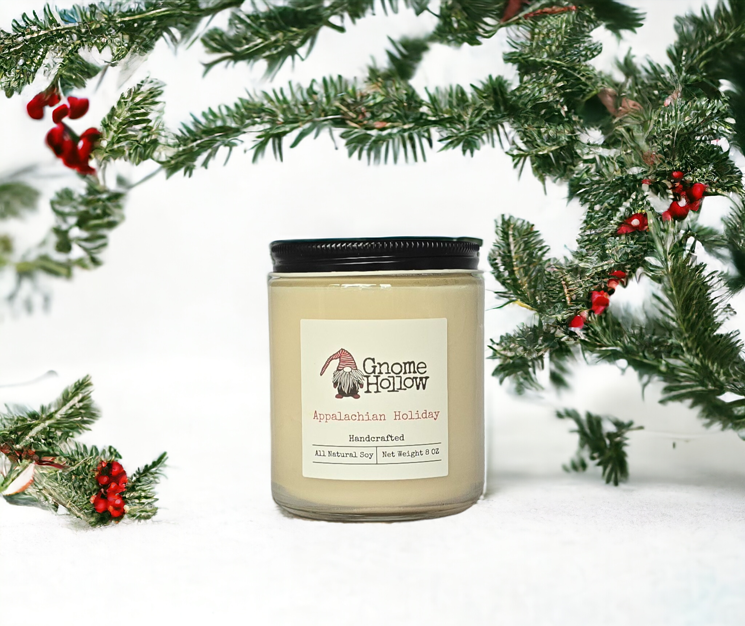 Gnome Hollow hand poured candle in a jar. Appalachian Holiday is sitting on snow surrounded by evergreen and berries