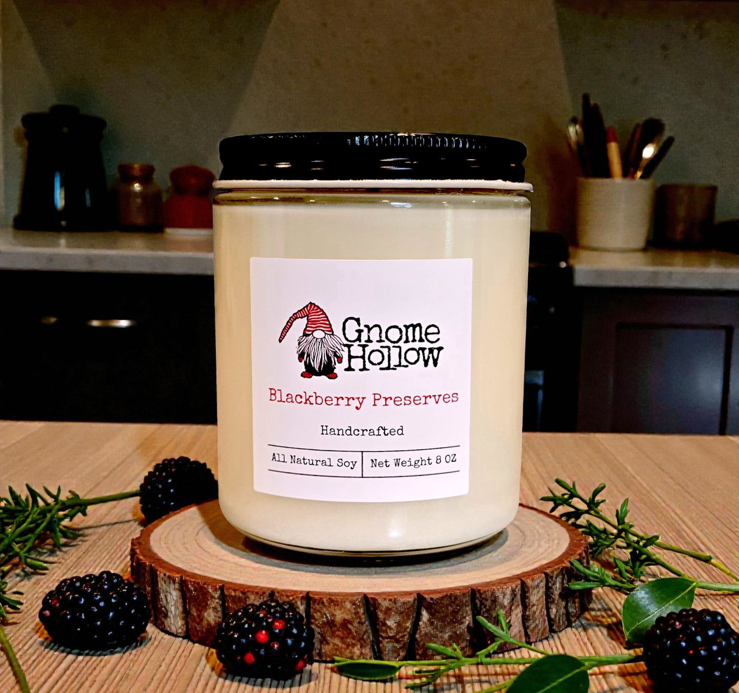 Gnome Hollow Blackberry Preserves candle on a wooden stand with blackberries and greenery in a kitchen setting