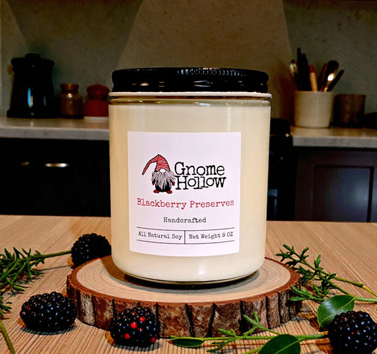 Gnome Hollow Blackberry Preserves candle on a wooden stand with blackberries and greenery in a kitchen setting