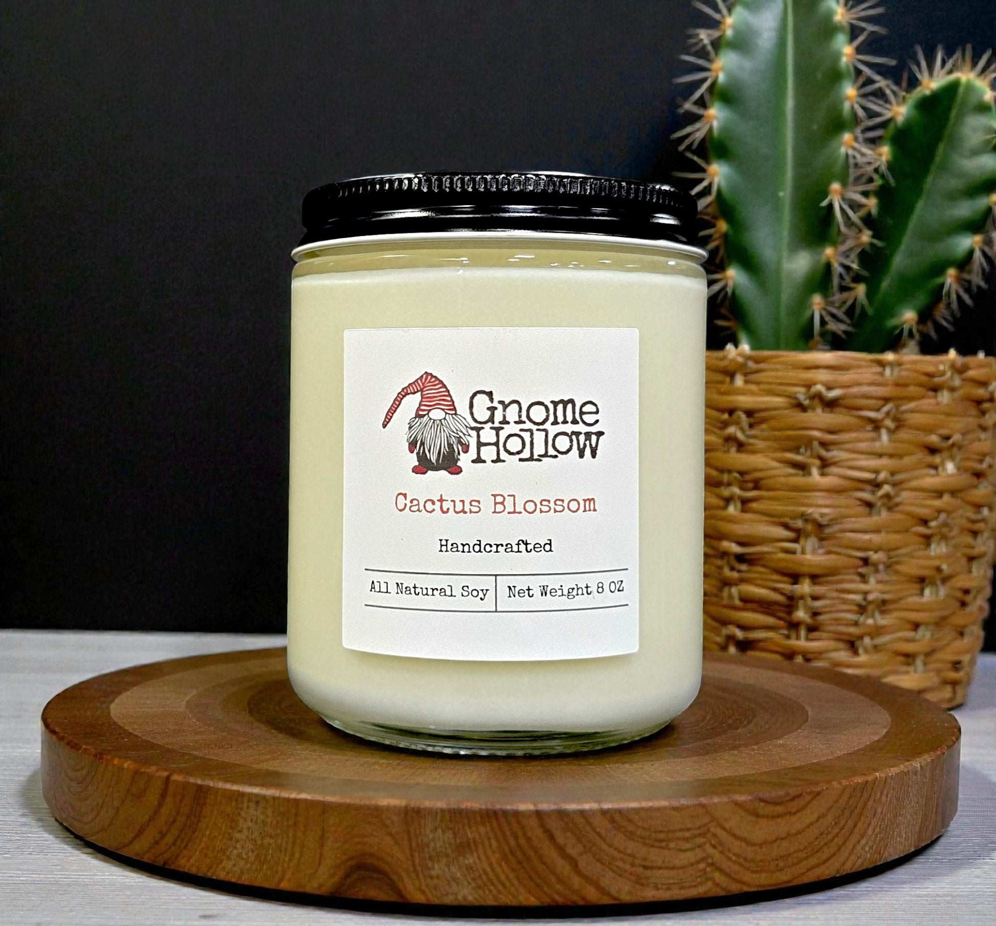 Gnome Hollow Cactus Blossom candle on a wooden stand with a cactus in the background