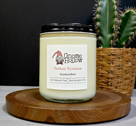 Gnome Hollow Cactus Blossom candle on a wooden stand with a cactus in the background