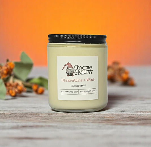 Clementine + Mint candle sitting on a wood surface with orange flowers displayed behind