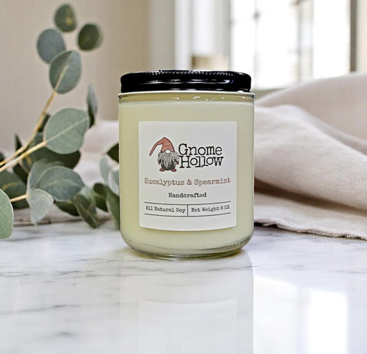 Gnome Hollow Eucalyptus & Spearmint candle placed on a marble surface with eucalyptus leaves in the background.