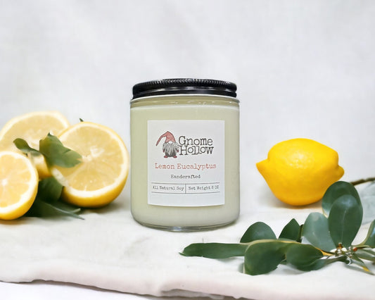 Lemon Eucalyptus candle accompanied by lemon halves and eucalyptus leaves on a white cloth.