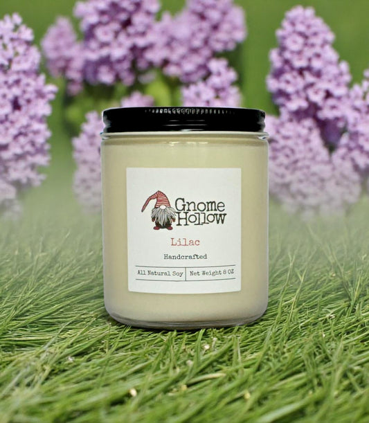 Lilac candle set on grass with lilac flowers in the background.