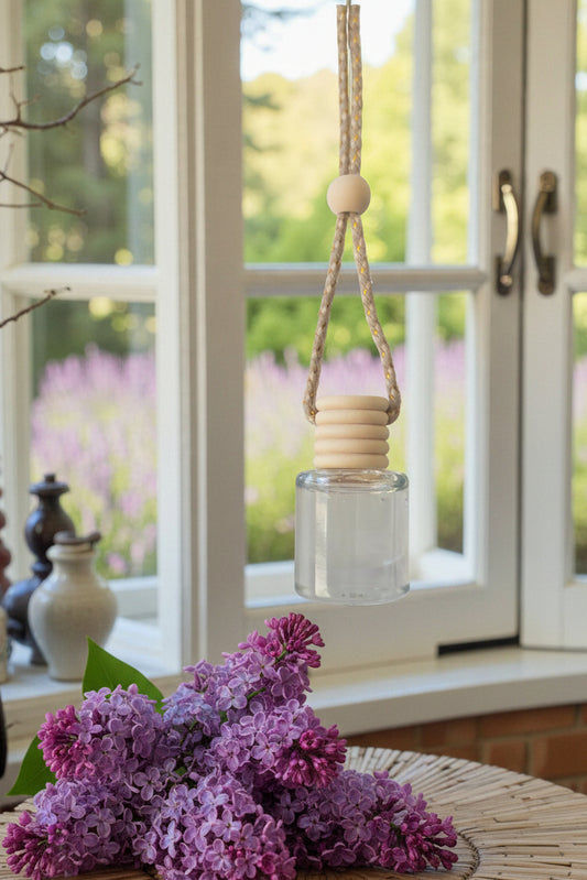 Decorative hanging bottle with wooden elements in front of a window with a view of greenery.