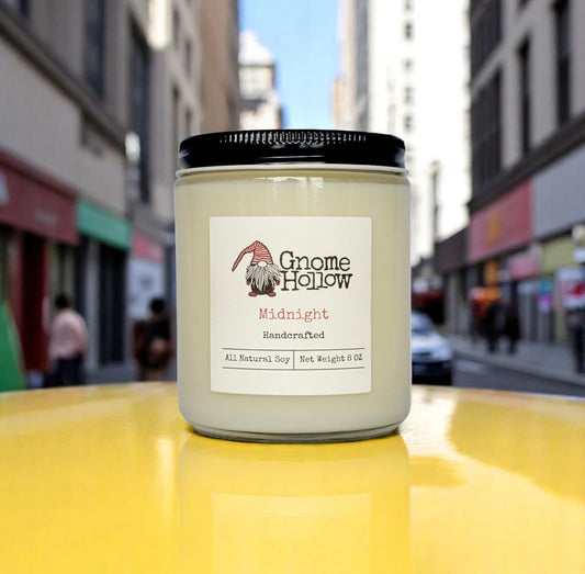 Midnight candle placed on a bright yellow surface with a city street in the background.