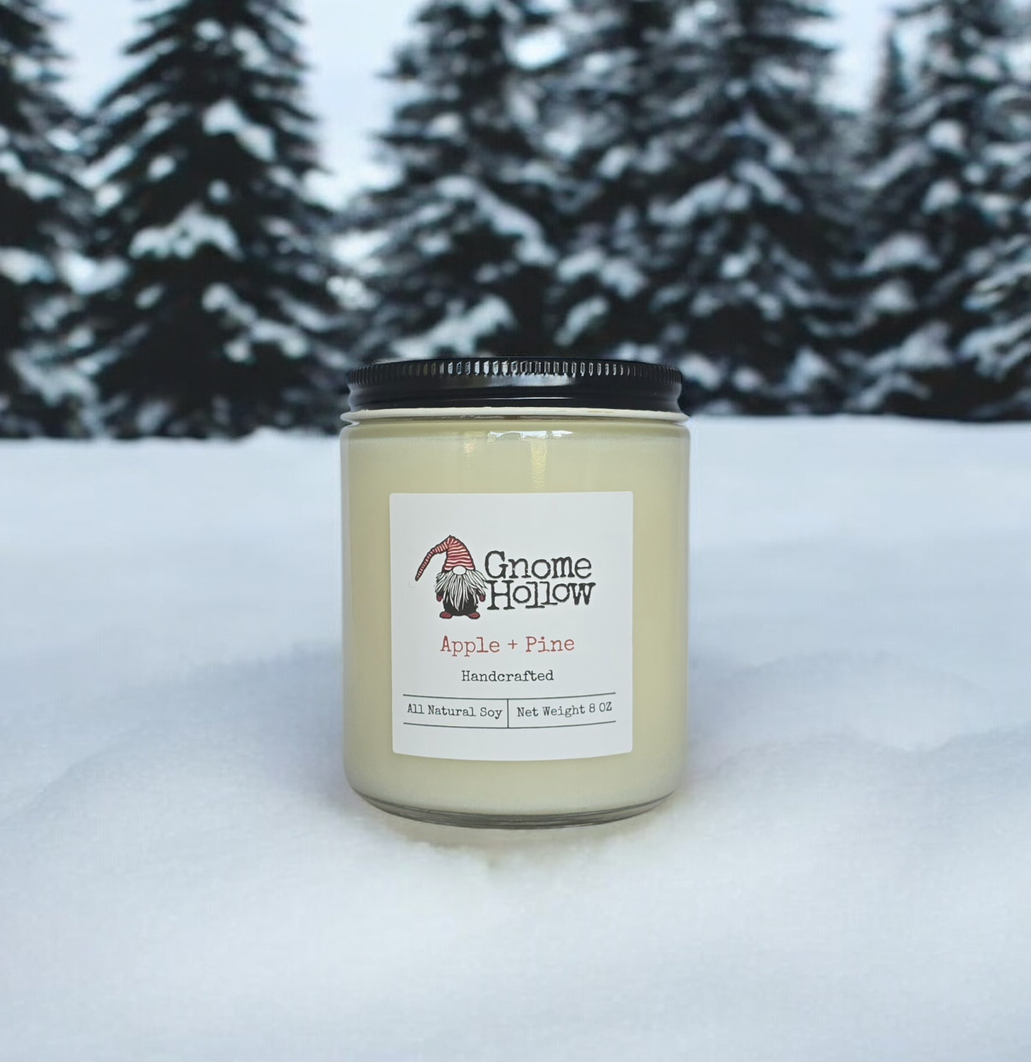 Gnome Hollow handmade candle in a jar. Apple + Pine is sitting in the snow with snow covered tree in the background