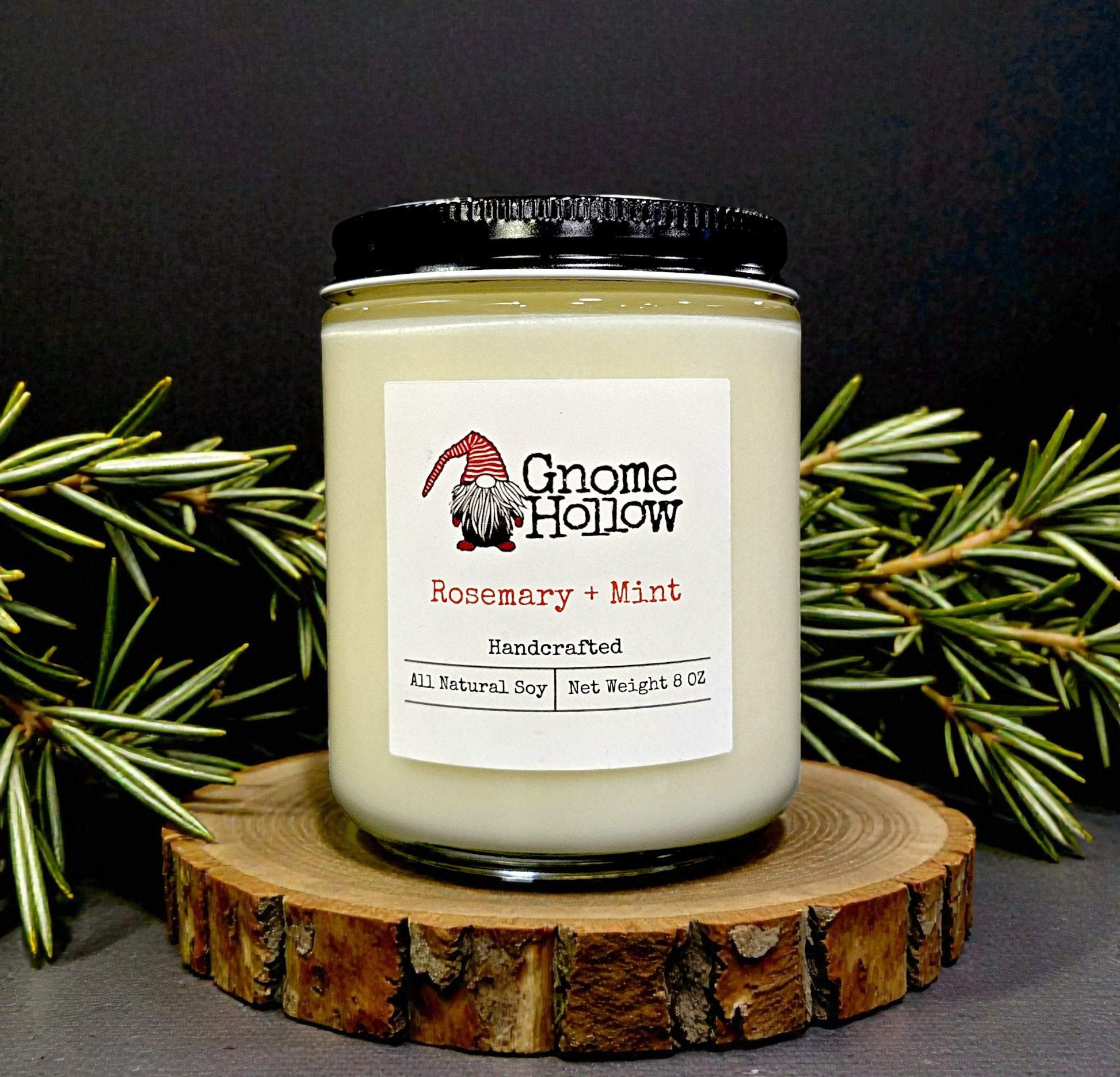 Gnome Hollow candle labeled 'Rosemary + Mint' on a wooden coaster with greenery in the background