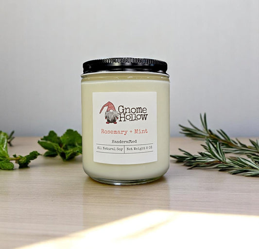 Gnome Hollow Rosemary & Mint candle sitting alongside some fresh rosemary and mint leaves.