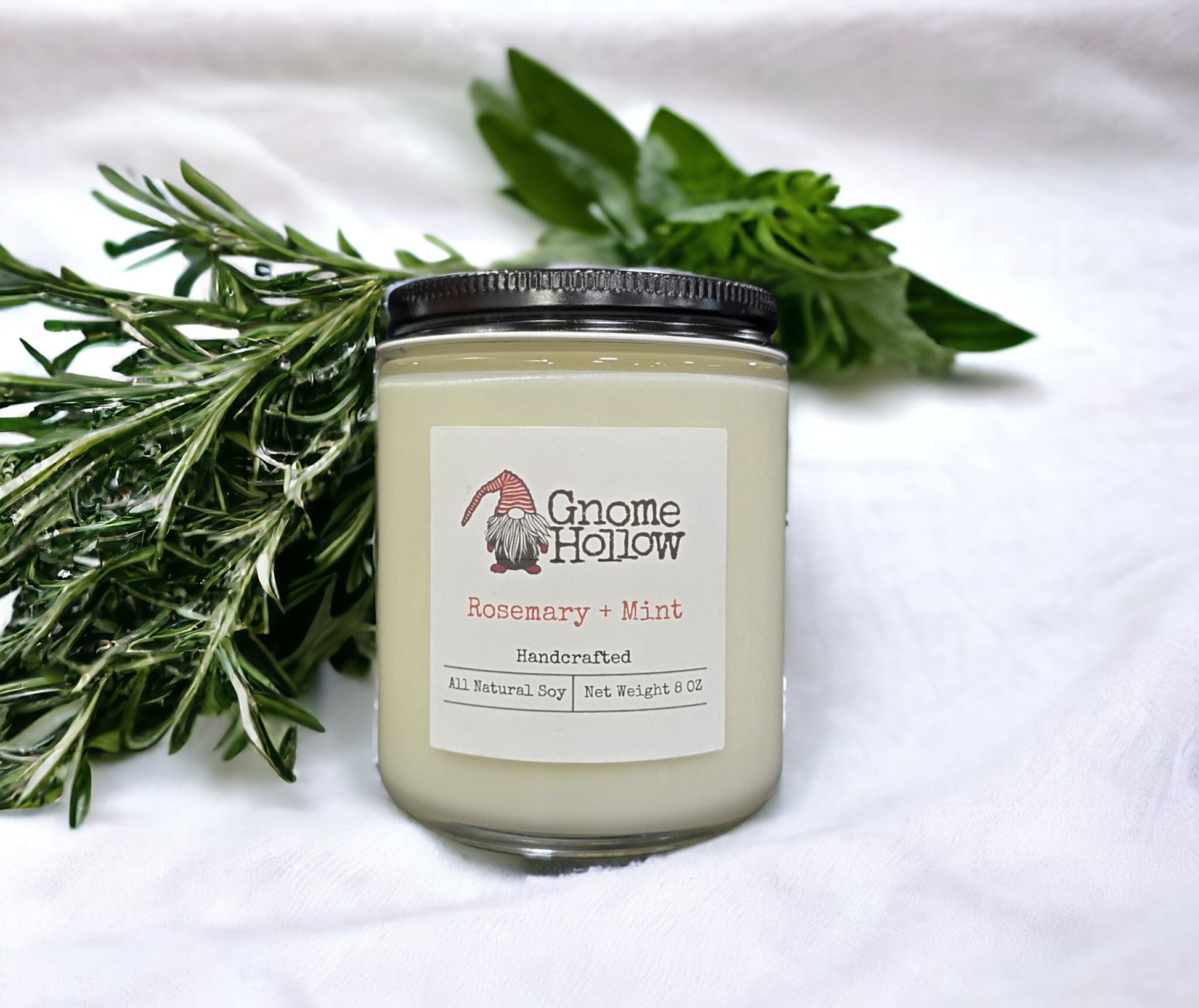 Rosemary + Mint candle in a white blanket with sprigs of mint surrounding it