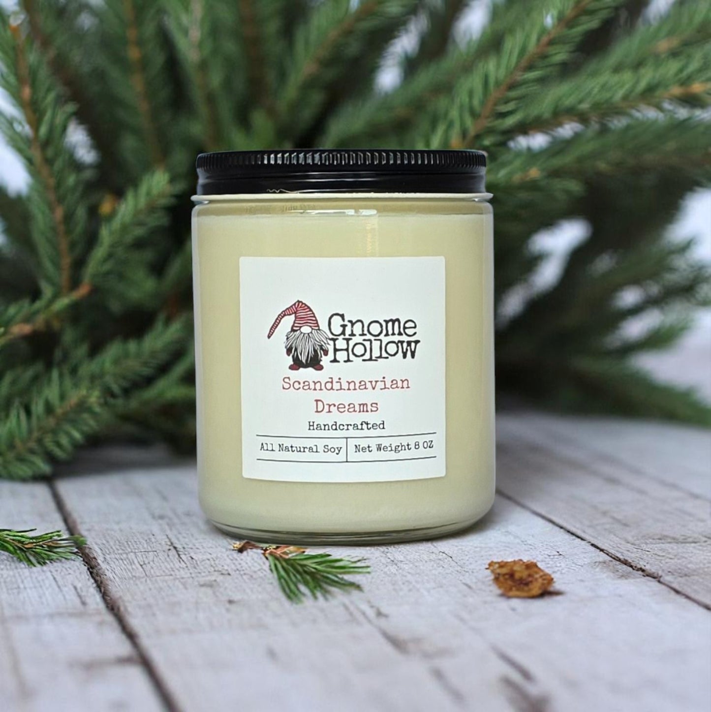 Scandinavian Dreams candle sitting on white wood planks with evergreen limbs in the background