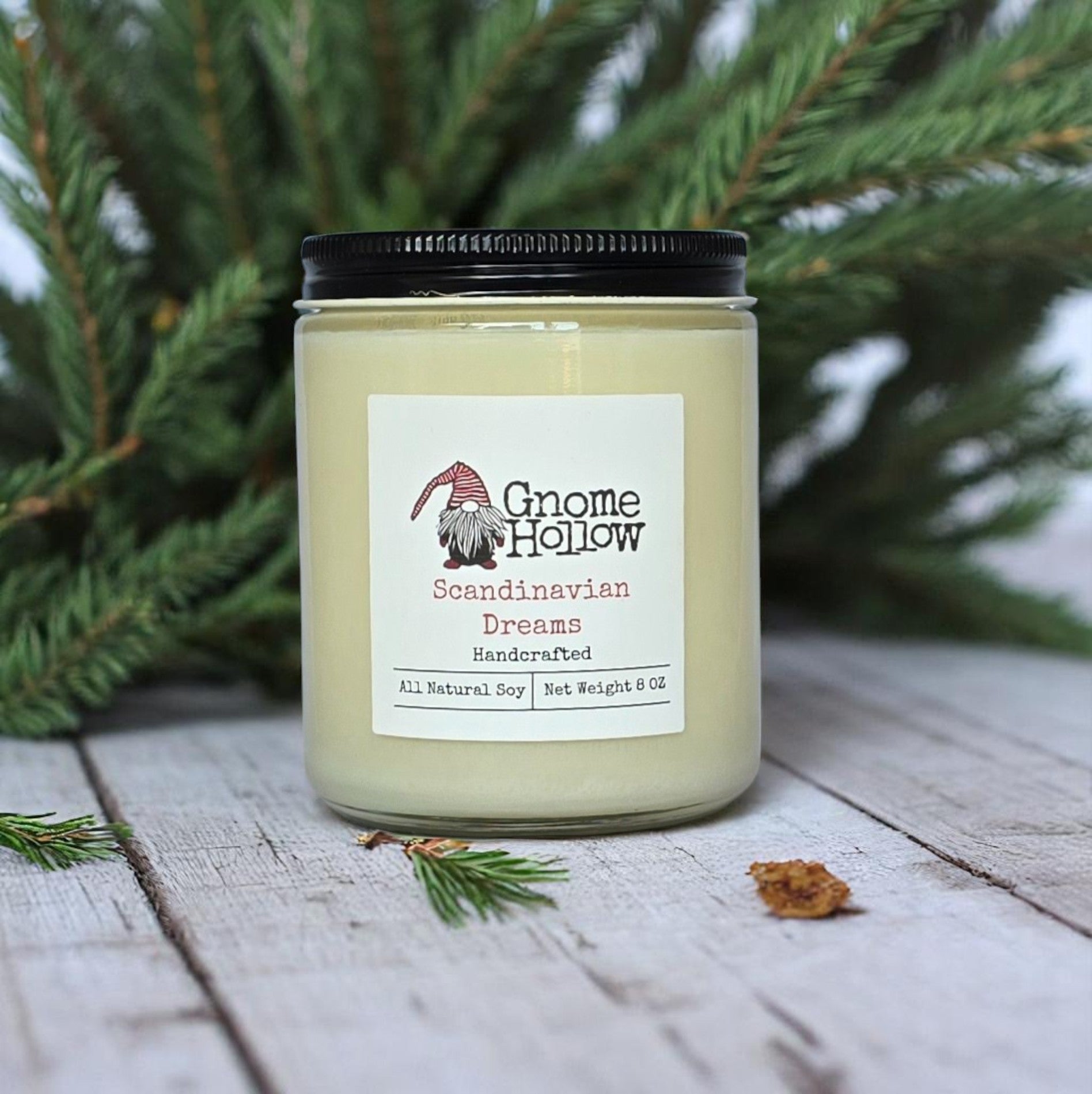 Scandinavian Dreams candle sitting on white wood planks with evergreen limbs in the background