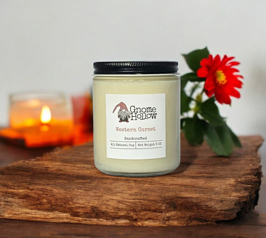 Western Corset candle on a wooden surface with a red flower in the background