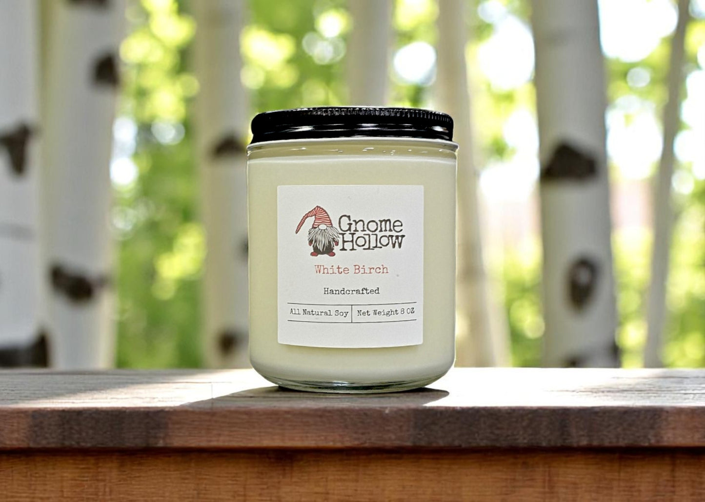 White Birch candle sitting on a wood railing with white birch trees in the background